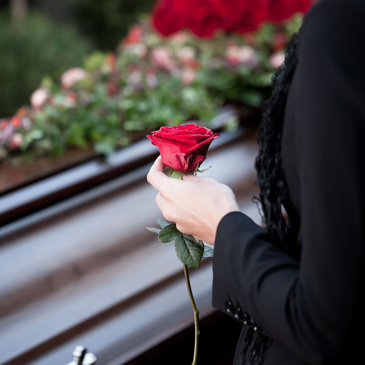 Eine Frau steht vor einem Sarg mit einer roten Rose